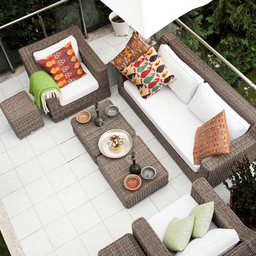 Wicker outdoor lounge with white cushions and orange and green complimenting cushions and cane joint coffee table in middle with candle sticks and accent color bowls, highlighting patio design options in the Fall.