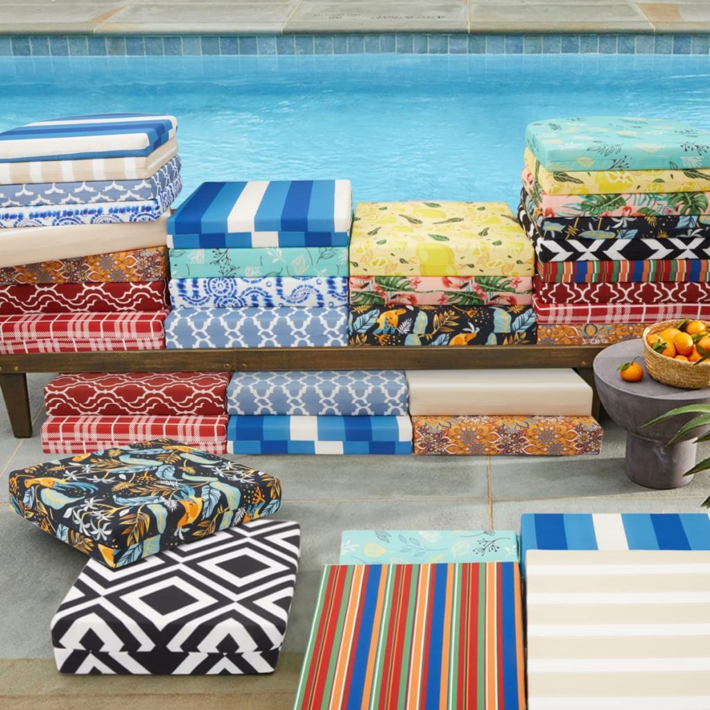 An array of square outdoor cushions in different colors next to a swimming pool as a consideration for getting waterproof outdoor cushions.